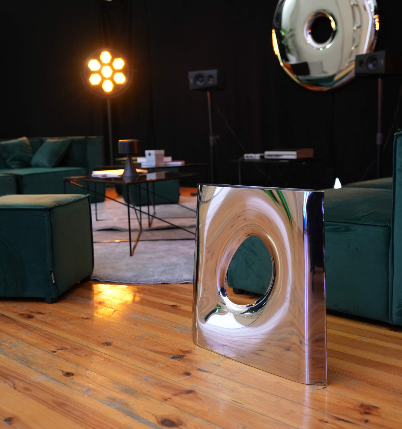 Reflective Karava vase by Zieta Studio, crafted from inflated inox steel, placed on a wooden floor in a contemporary lounge with green furniture.